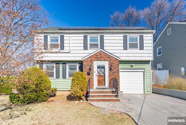 colonial home with driveway, fence, an attached garage, brick siding, and solar panels