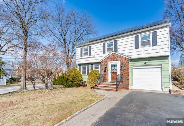 colonial house featuring a front yard, driveway, solar panels, an attached garage, and brick siding