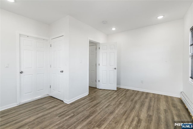 unfurnished bedroom featuring a baseboard heating unit, recessed lighting, baseboards, and wood finished floors