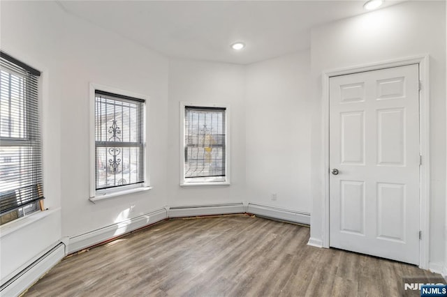 spare room with plenty of natural light, a baseboard radiator, baseboards, and wood finished floors