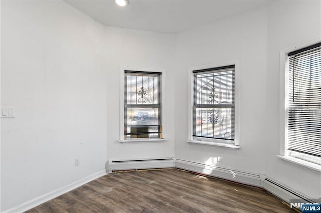 unfurnished room with a baseboard heating unit, baseboards, and wood finished floors