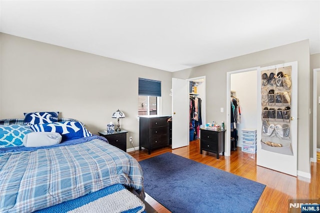 bedroom with a closet, baseboards, a walk in closet, and wood finished floors