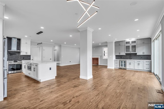 kitchen with decorative columns, wall chimney exhaust hood, wine cooler, appliances with stainless steel finishes, and crown molding