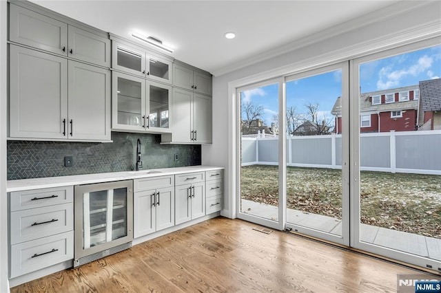 interior space with wine cooler, light wood-style flooring, a sink, tasteful backsplash, and indoor wet bar