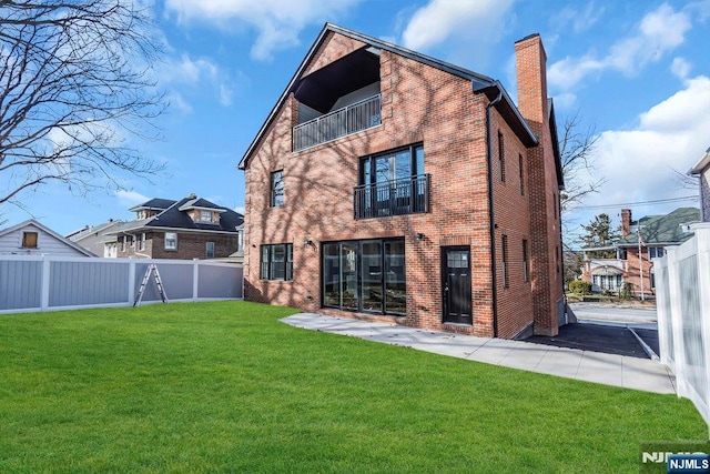 back of property featuring a balcony, a chimney, fence private yard, a yard, and brick siding