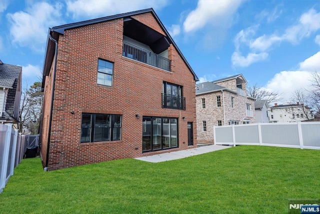 rear view of property featuring brick siding, a yard, a balcony, and a fenced backyard