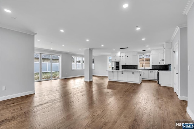 unfurnished living room featuring baseboards, ornamental molding, wood finished floors, and recessed lighting