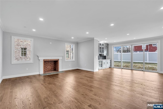 unfurnished living room with a healthy amount of sunlight, a fireplace with flush hearth, ornamental molding, and wood finished floors