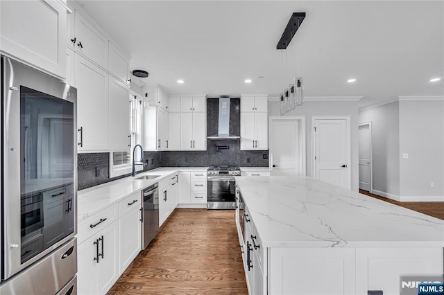 kitchen with wall chimney exhaust hood, a kitchen island, appliances with stainless steel finishes, a sink, and backsplash