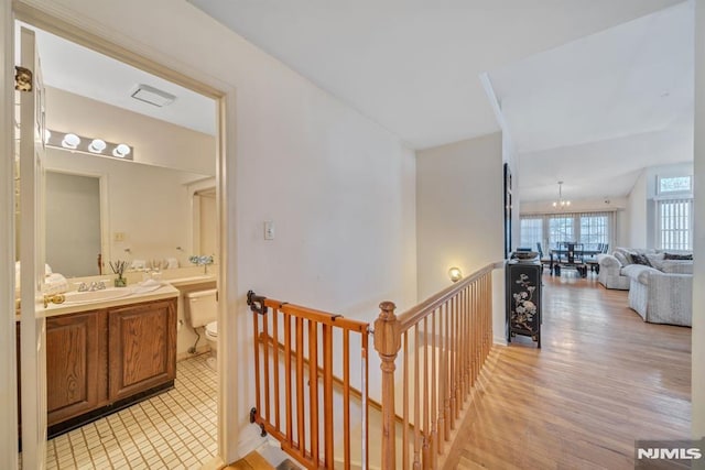 corridor featuring a sink, light wood finished floors, and an upstairs landing