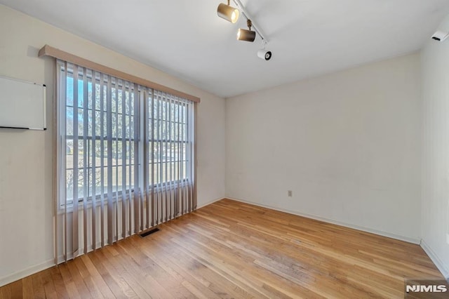 empty room featuring visible vents, rail lighting, and hardwood / wood-style flooring