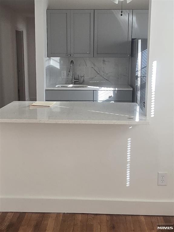 kitchen featuring wood finished floors, light stone countertops, gray cabinets, a sink, and tasteful backsplash