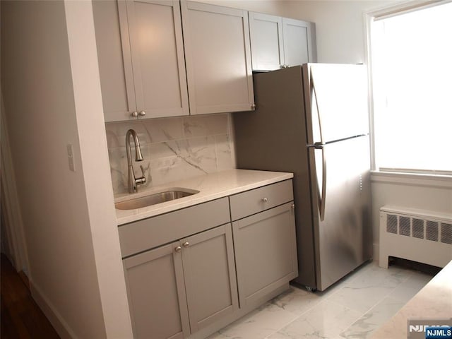 kitchen with radiator heating unit, gray cabinets, a sink, marble finish floor, and backsplash