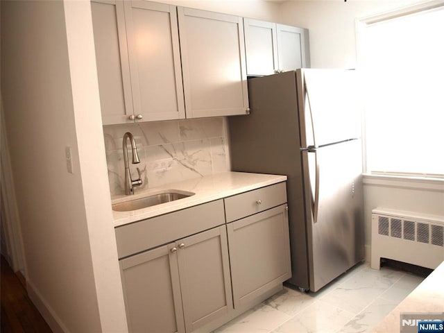 kitchen with radiator heating unit, gray cabinetry, a sink, marble finish floor, and backsplash