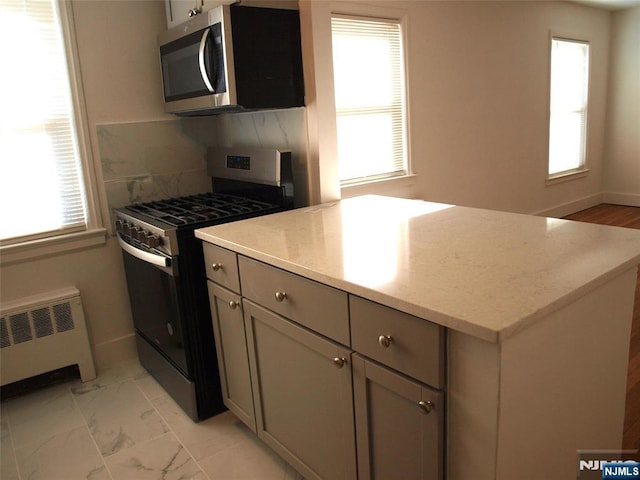 kitchen with backsplash, gray cabinetry, radiator heating unit, appliances with stainless steel finishes, and marble finish floor