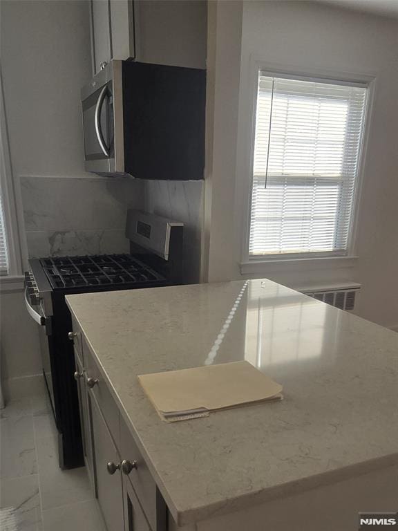 kitchen with stainless steel microwave, light stone countertops, decorative backsplash, marble finish floor, and gas stove