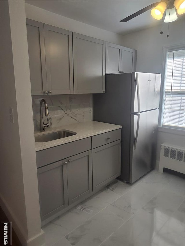 kitchen with radiator heating unit, freestanding refrigerator, a sink, gray cabinetry, and marble finish floor