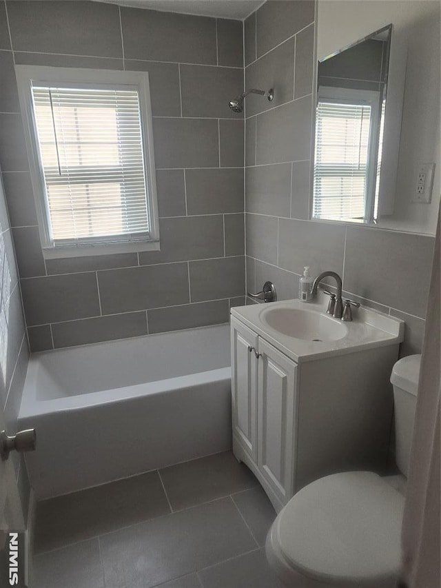 bathroom with tile patterned flooring, tile walls, toilet, vanity, and  shower combination