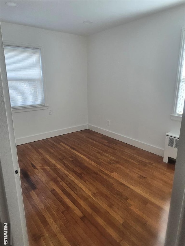 spare room featuring radiator, dark wood-style floors, and baseboards