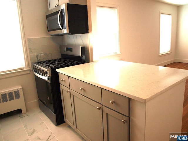 kitchen featuring a wealth of natural light, radiator heating unit, marble finish floor, and appliances with stainless steel finishes