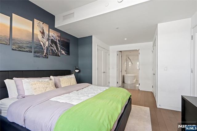 bedroom with baseboards, connected bathroom, visible vents, and hardwood / wood-style floors