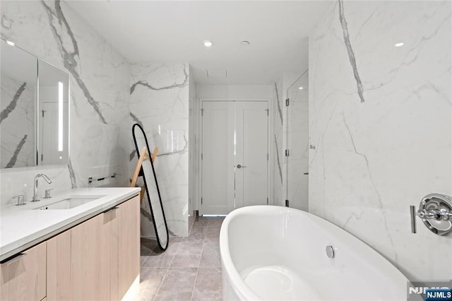 full bathroom featuring stone wall, a soaking tub, vanity, and tile walls