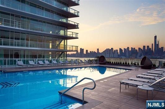 pool at dusk with a view of city, a patio, and a community pool