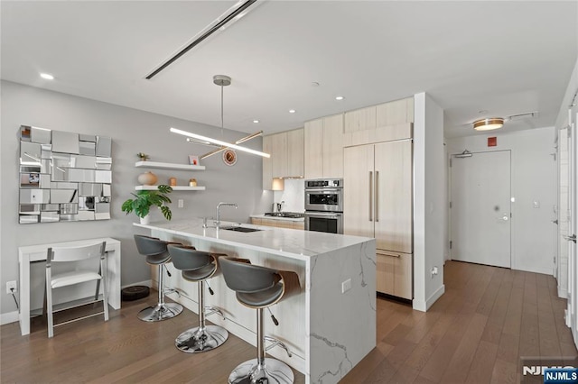 kitchen with wood finished floors, a sink, appliances with stainless steel finishes, modern cabinets, and a kitchen bar