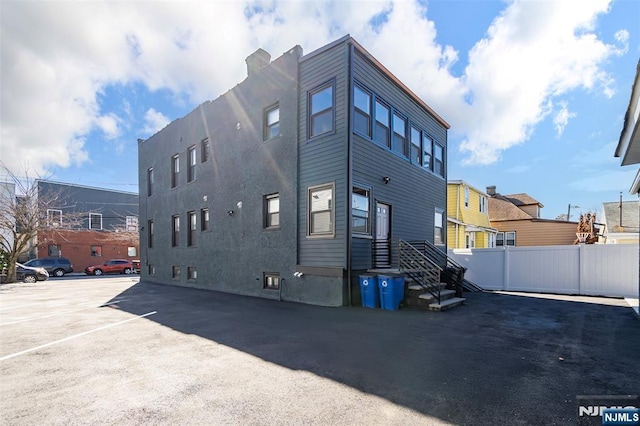 back of house featuring uncovered parking, fence, and stucco siding