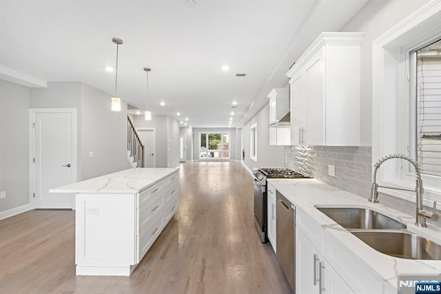 kitchen with light wood finished floors, appliances with stainless steel finishes, open floor plan, a sink, and backsplash