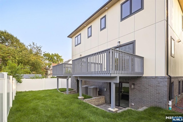 back of property with brick siding, a lawn, fence, and central air condition unit