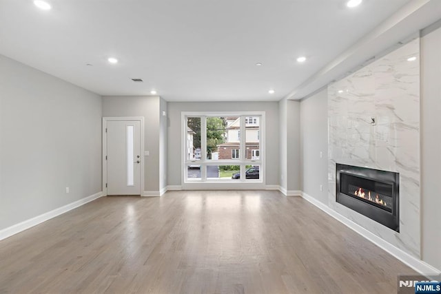 unfurnished living room featuring recessed lighting, a fireplace, baseboards, and wood finished floors