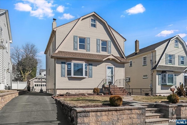 colonial inspired home with a shingled roof, a gambrel roof, a detached garage, aphalt driveway, and fence