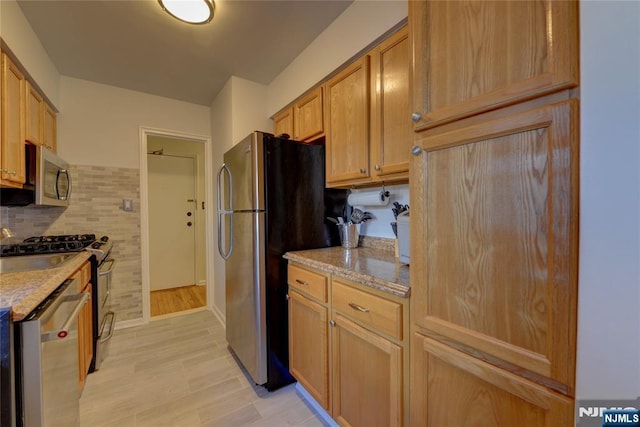 kitchen featuring appliances with stainless steel finishes, light wood-type flooring, light stone counters, and tasteful backsplash