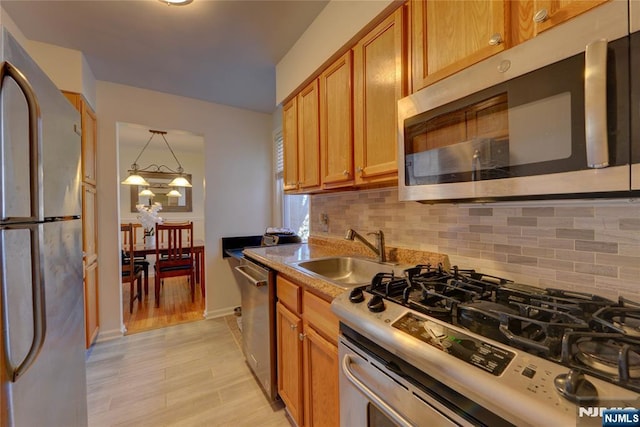 kitchen featuring a sink, light wood-style floors, appliances with stainless steel finishes, brown cabinets, and tasteful backsplash