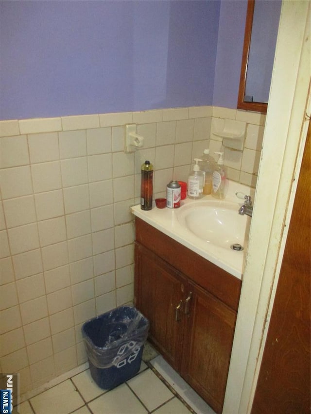 half bath with a wainscoted wall, tile patterned flooring, tile walls, and vanity