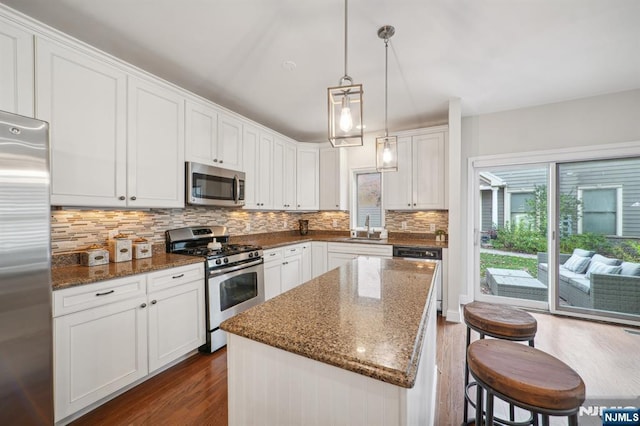 kitchen featuring dark wood-style floors, a center island, stainless steel appliances, decorative backsplash, and a sink