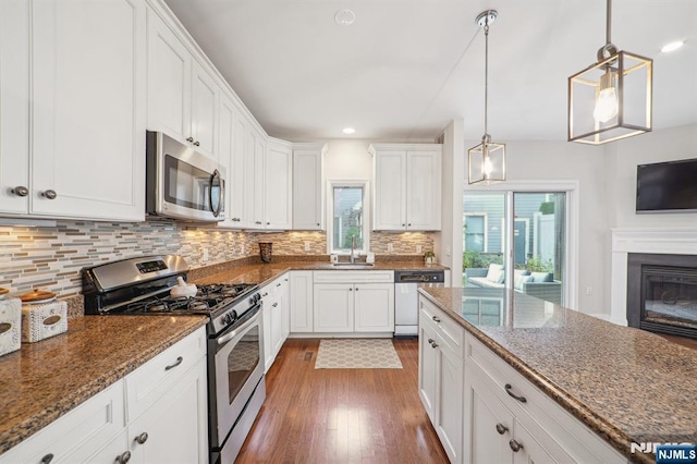 kitchen with white cabinets, decorative backsplash, a glass covered fireplace, stainless steel appliances, and a sink