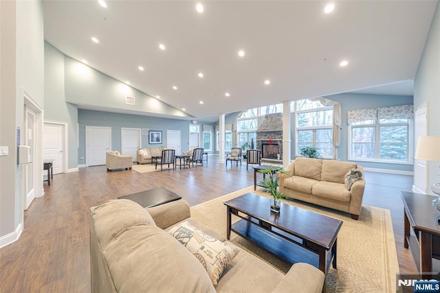 living area featuring high vaulted ceiling, recessed lighting, a stone fireplace, and wood finished floors