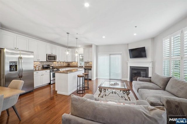 living area featuring baseboards, dark wood-style flooring, a glass covered fireplace, and recessed lighting