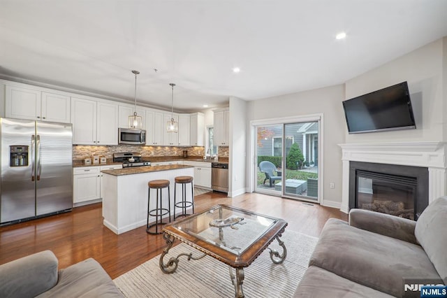 living area featuring recessed lighting, baseboards, wood finished floors, and a glass covered fireplace