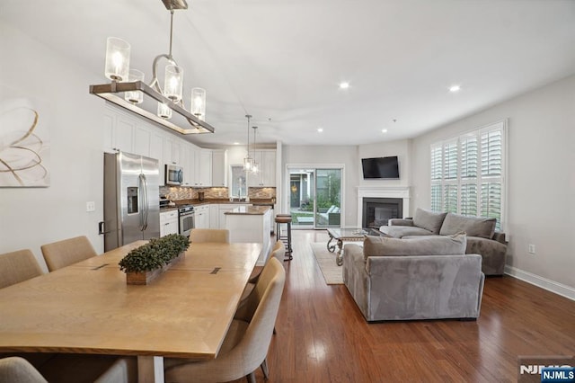 dining room featuring an inviting chandelier, baseboards, dark wood-type flooring, and a glass covered fireplace