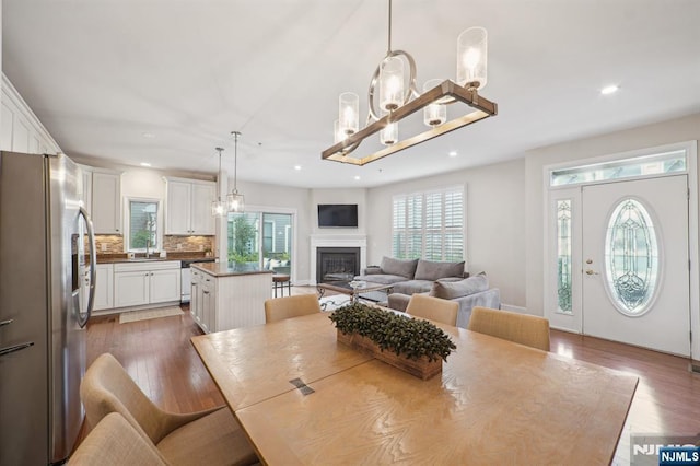 dining area featuring dark wood-style floors, a glass covered fireplace, a notable chandelier, and recessed lighting