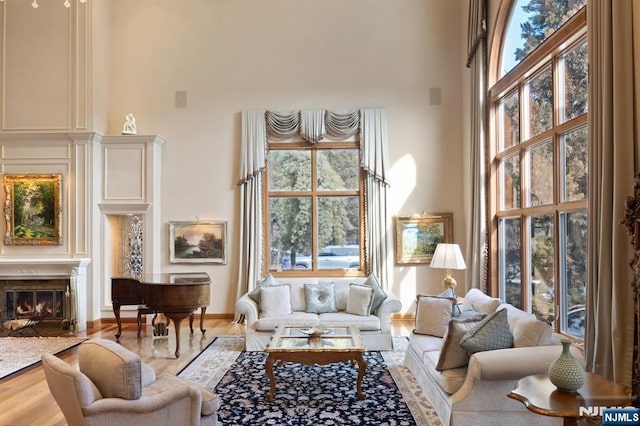 living room with a high ceiling, baseboards, wood finished floors, and a high end fireplace