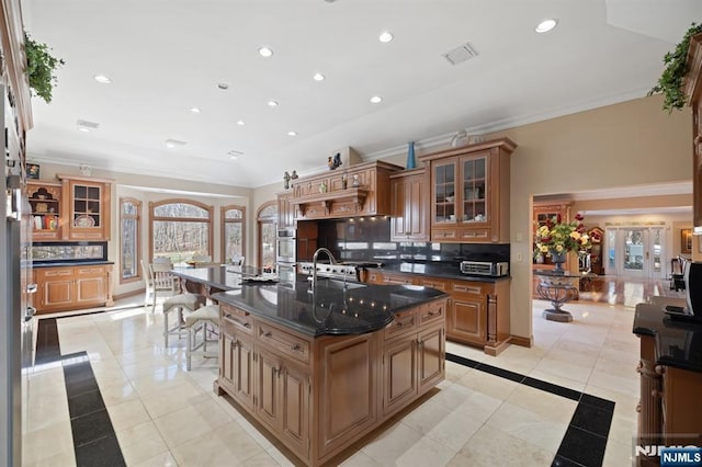 kitchen with visible vents, a center island with sink, ornamental molding, and backsplash