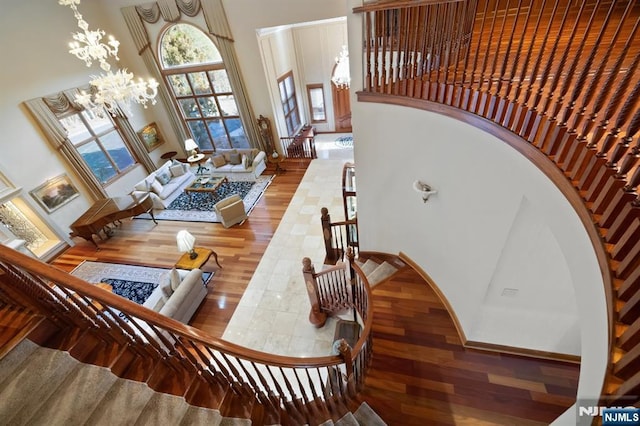 stairs with wood finished floors, a towering ceiling, and an inviting chandelier