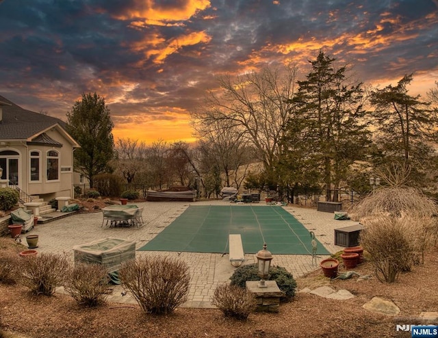 pool at dusk with entry steps, a covered pool, a patio, and a diving board