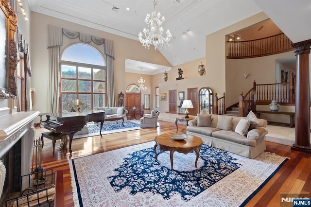 living room with decorative columns, wood finished floors, stairs, crown molding, and a notable chandelier