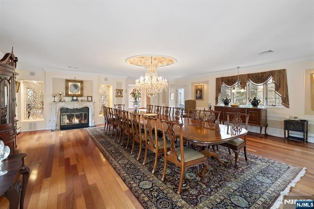 dining room featuring a chandelier, wood finished floors, visible vents, a glass covered fireplace, and crown molding