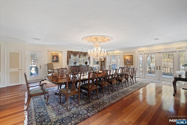 dining area featuring visible vents, ornamental molding, wood finished floors, an inviting chandelier, and french doors